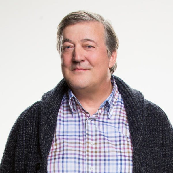 Stephen Fry smiling and wearing a checkered shirt and cardigan